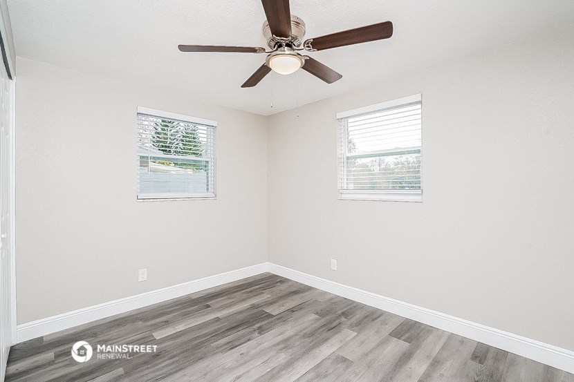 the spacious living room with wood flooring and a ceiling fan
