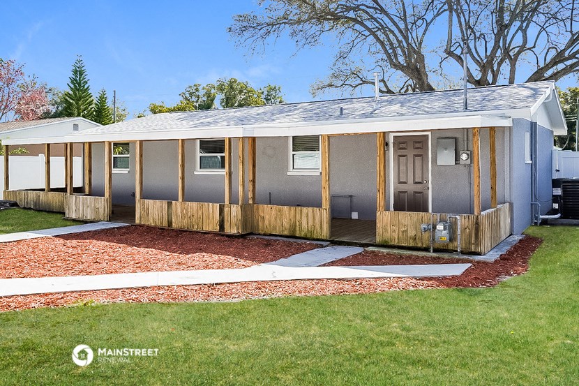 a small house with a porch and a yard with a lawn and a tree