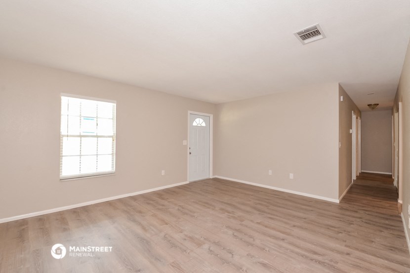 the spacious living room with hardwood floors and white walls