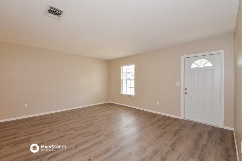 the spacious living room with wood flooring and a white door
