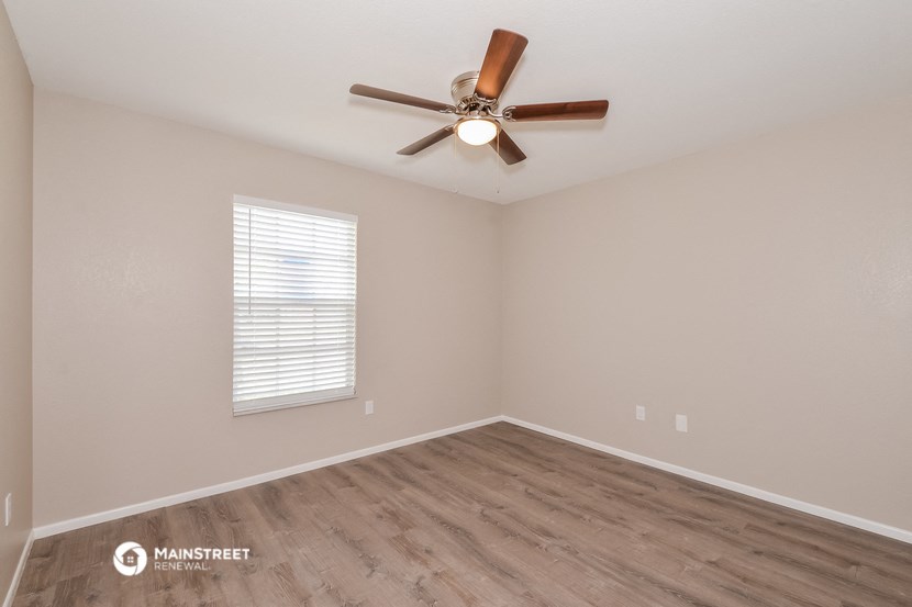 the spacious living room with wood flooring and a ceiling fan