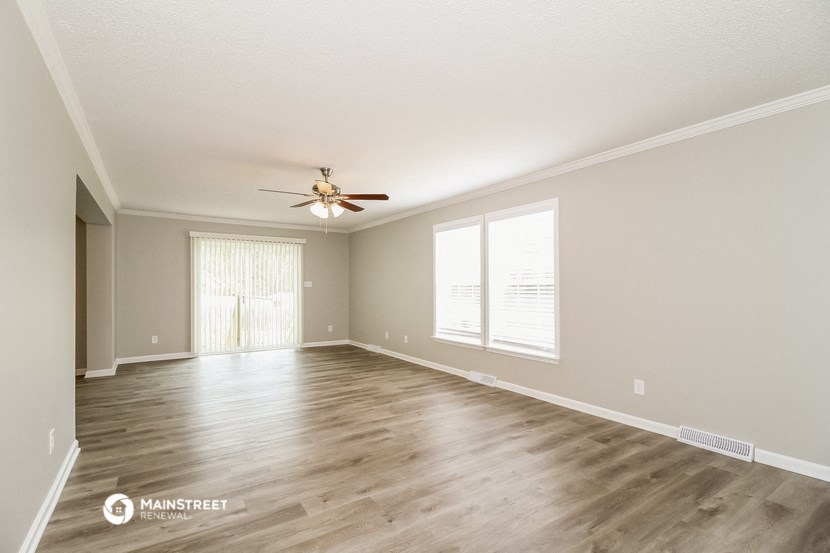 the spacious living room with hardwood floors and a ceiling fan