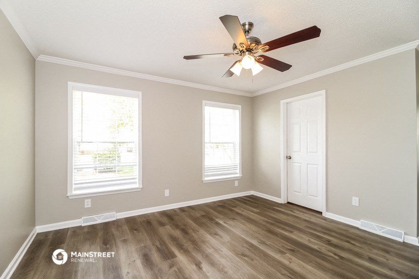 the spacious living room with a ceiling fan and two windows