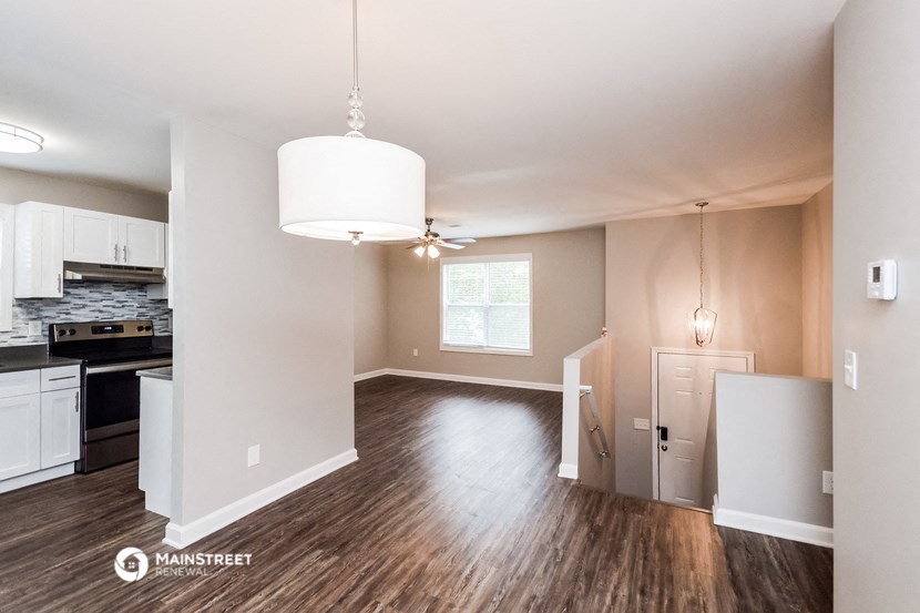 an empty living room and kitchen with hardwood flooring and white walls