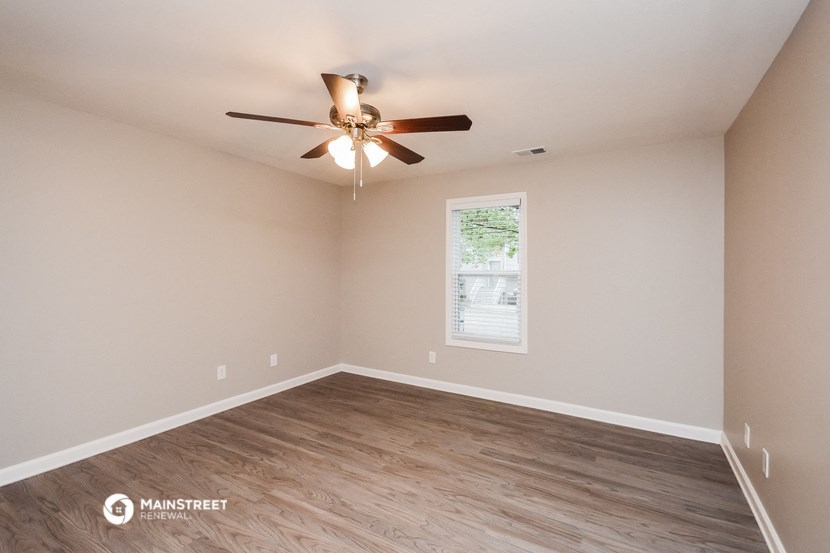 the spacious living room with hardwood flooring and a ceiling fan