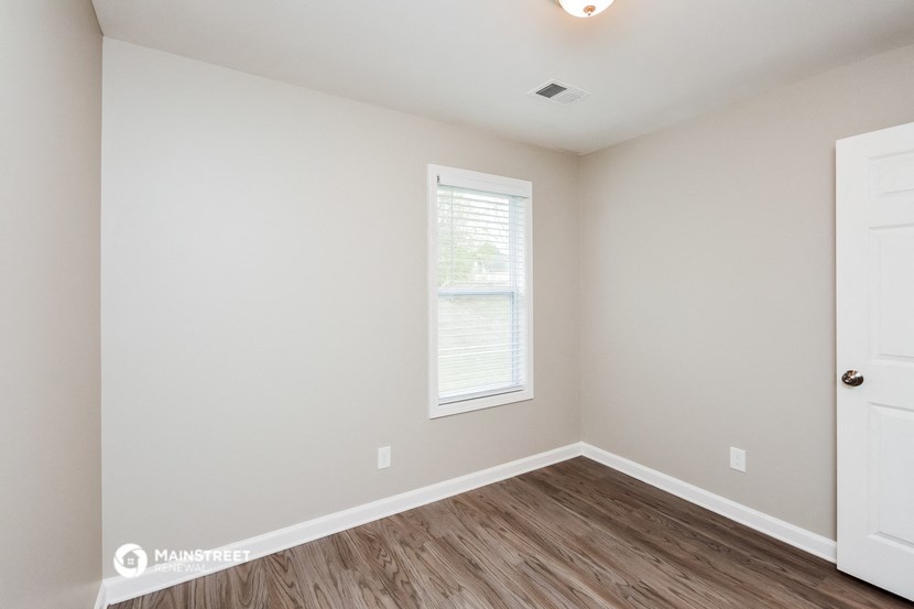 a bedroom with white walls and wood flooring and a window
