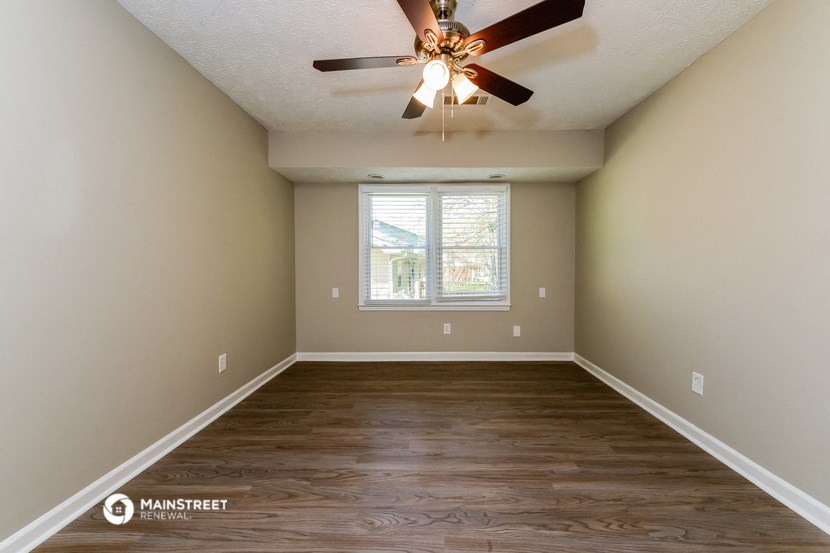 the spacious living room with hardwood flooring and a ceiling fan