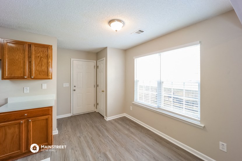 the living room and kitchen of an apartment with a large window and wooden floors