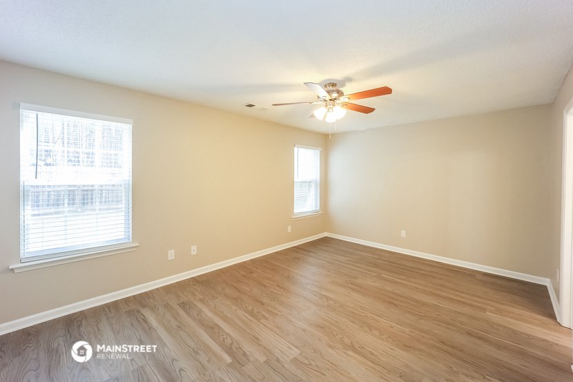the spacious living room with hardwood flooring and a ceiling fan