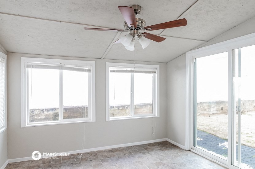 an empty room with a ceiling fan and three windows