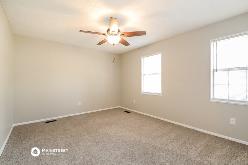 the spacious living room with ceiling fan and two windows