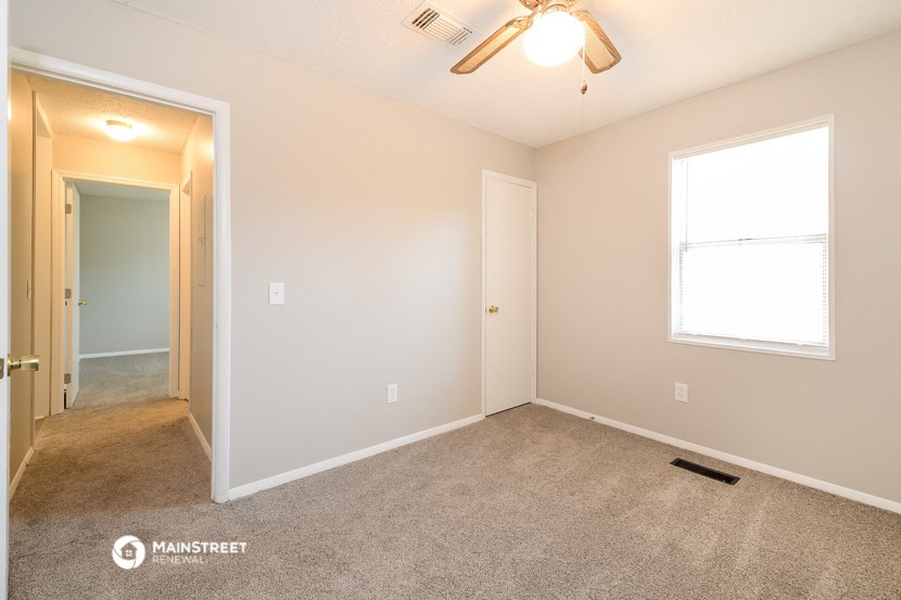 the spacious living room with carpeted flooring and a ceiling fan