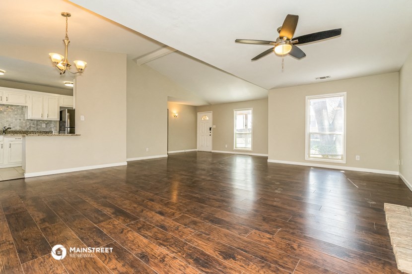an empty living room with a ceiling fan and a kitchen