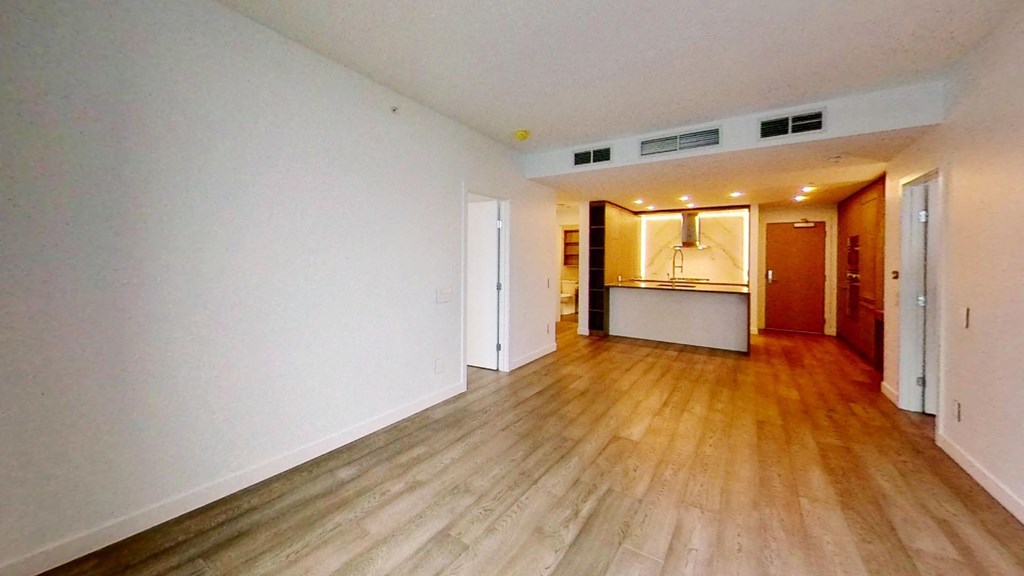 an empty living room and kitchen with wood floors and white walls
