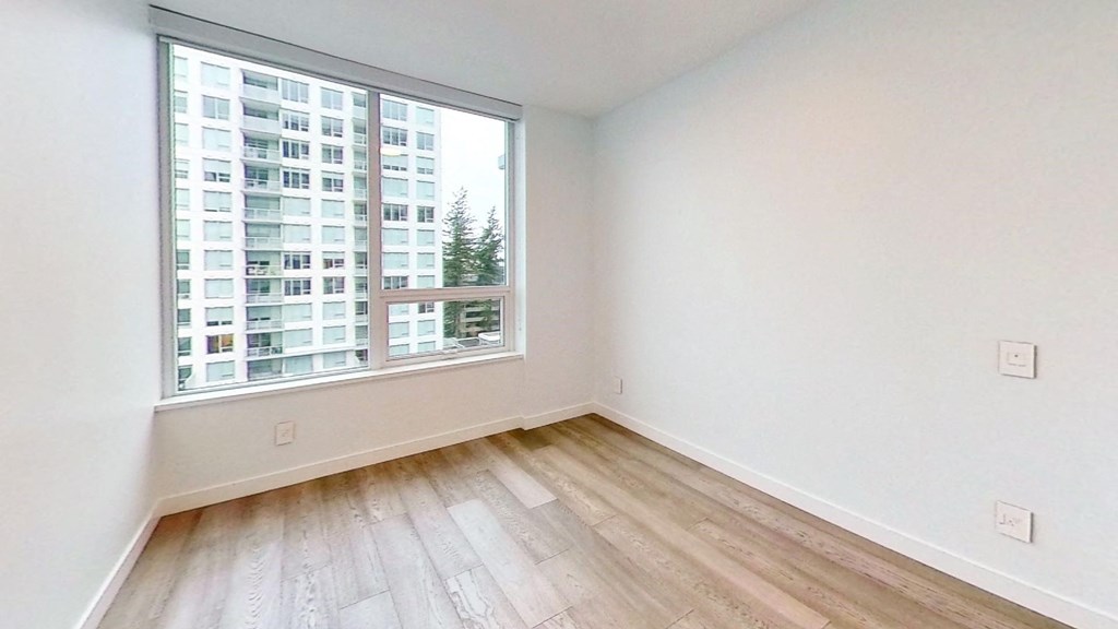 an empty bedroom with a large window and wood flooring