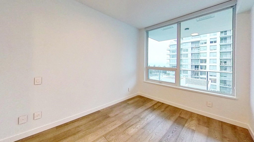 an empty bedroom with a large window and wood flooring