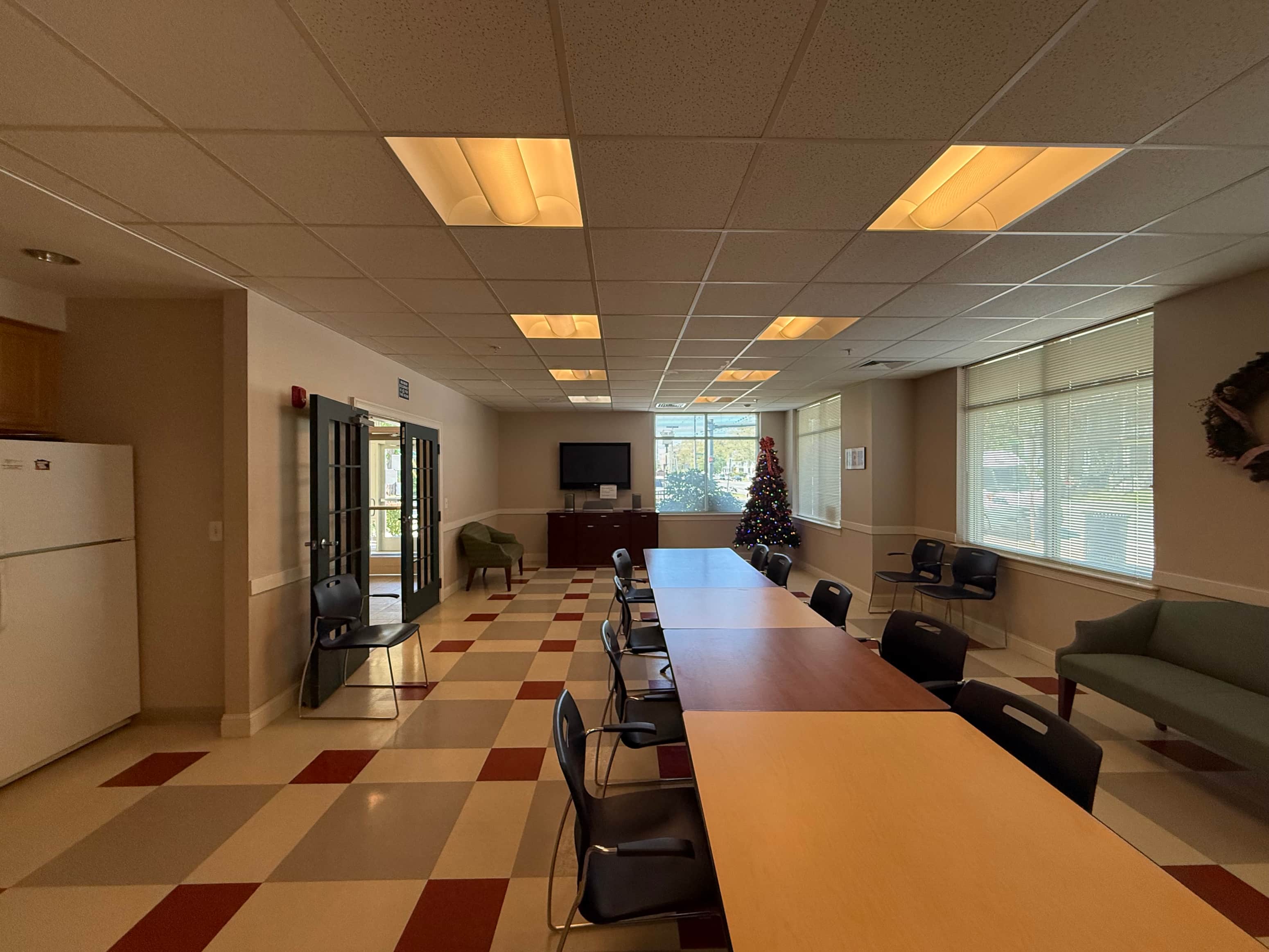 A room with a long table and chairs, a television, and a Christmas tree.