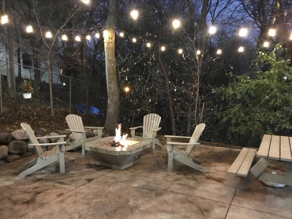 a patio with a fire pit and chairs and lights