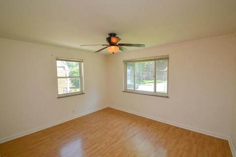 A room with a ceiling fan and two windows.