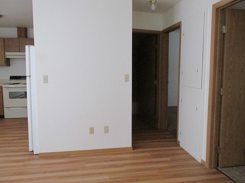 an empty room with a wooden floor and a door to a kitchen
