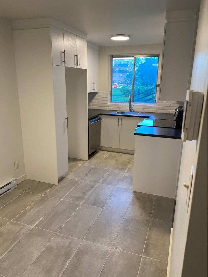 an empty kitchen with white cabinets and a window
