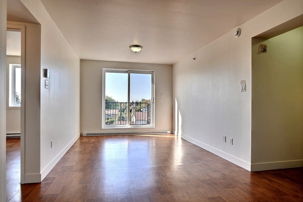 an empty living room with a large window and wooden floors