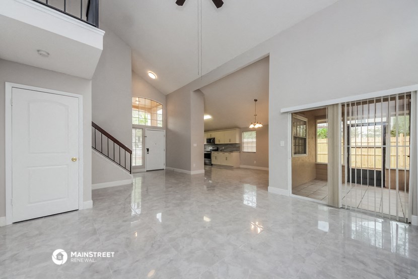 an empty living room with a staircase and a door to a kitchen