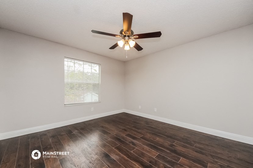 the spacious living room with wood flooring and a ceiling fan