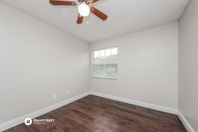 the spacious living room with wood flooring and a ceiling fan