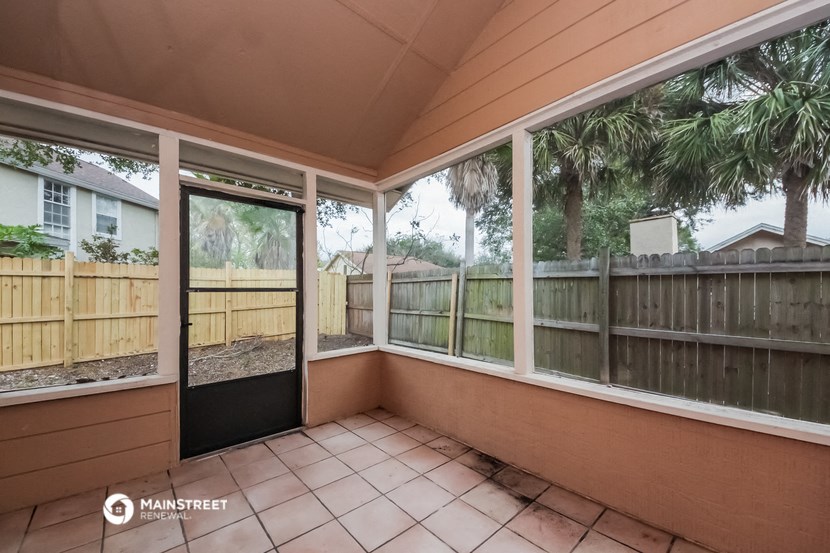 a covered porch with large windows and a wooden fence