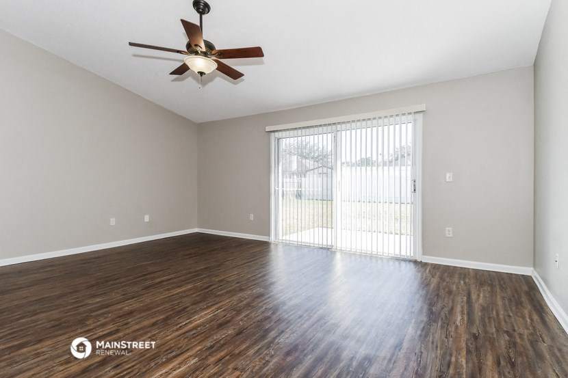 the spacious living room with a large window and a ceiling fan