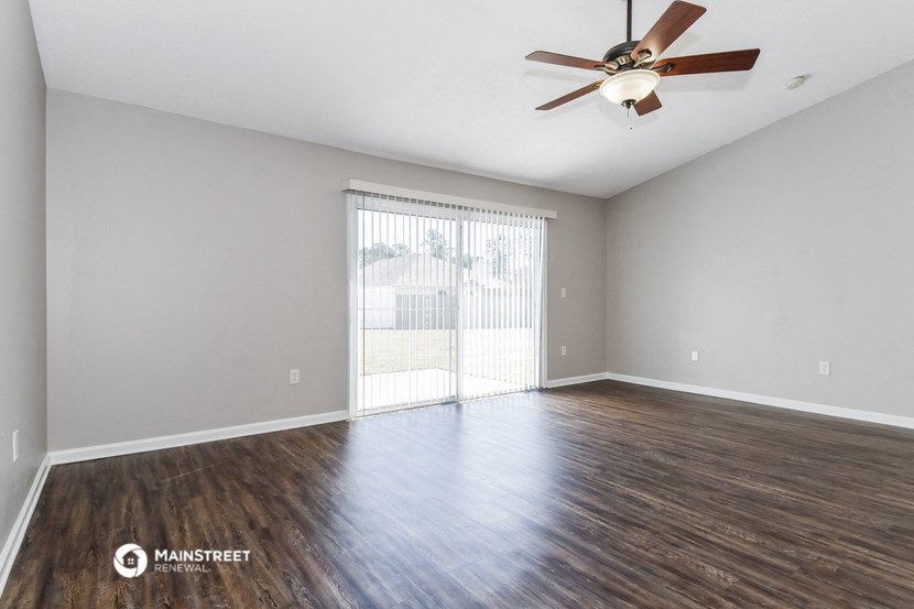 the spacious living room with a large window and ceiling fan