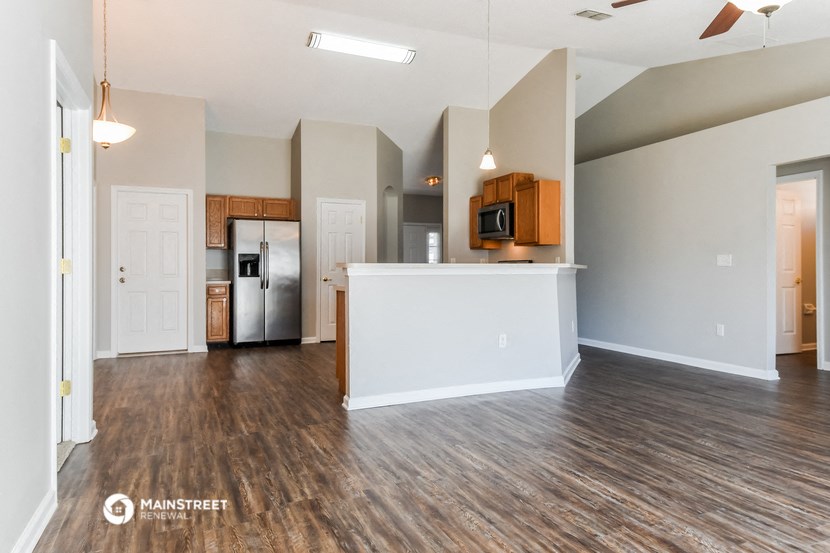 an empty living room with a kitchen and a hard wood floor