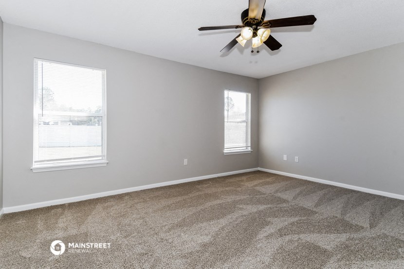 the spacious living room with two windows and a ceiling fan