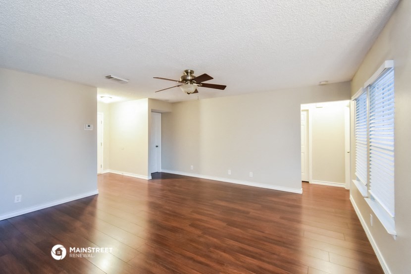an empty living room with wood floors and a ceiling fan