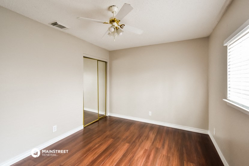 the spacious living room with hardwood flooring and a ceiling fan