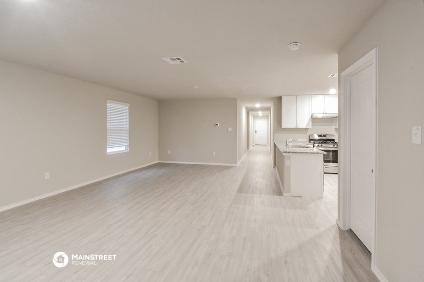 an empty living room with a kitchen in the background