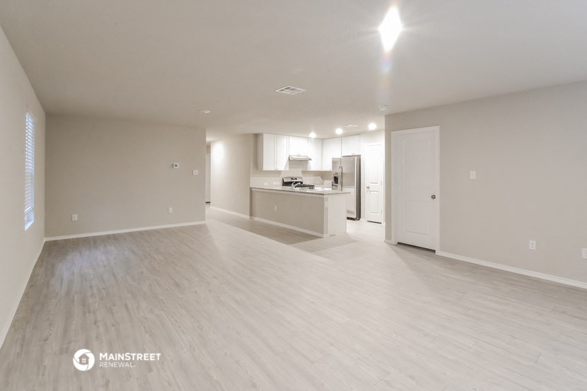 an empty living room with a kitchen in the background