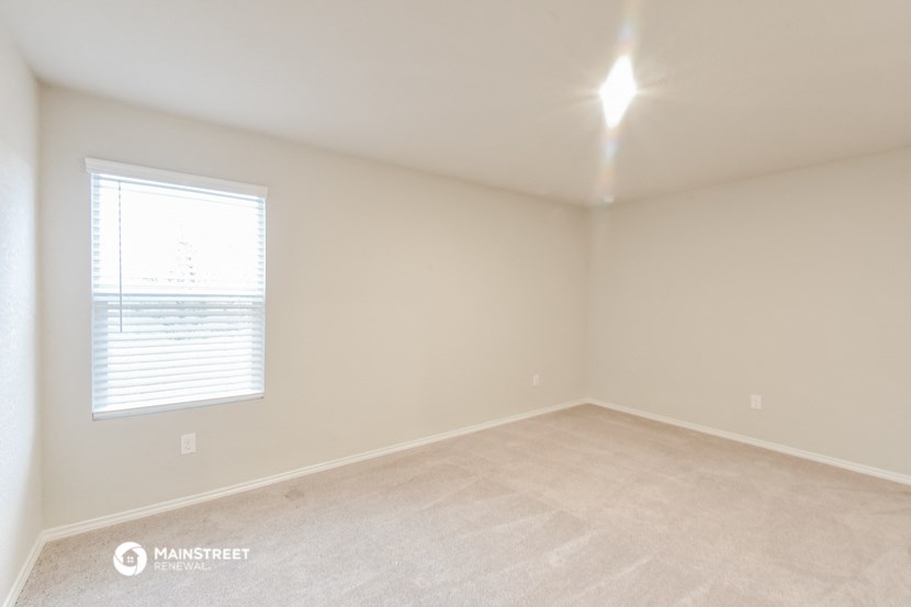 an empty room with a window and beige carpet