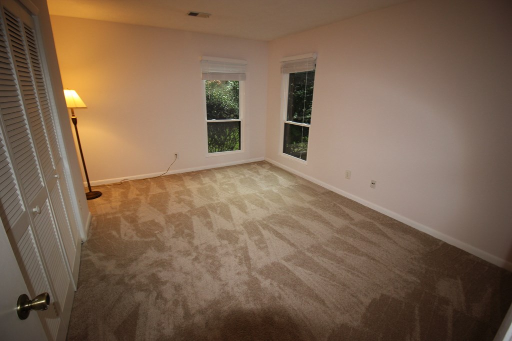 a empty living room with carpet and two windows