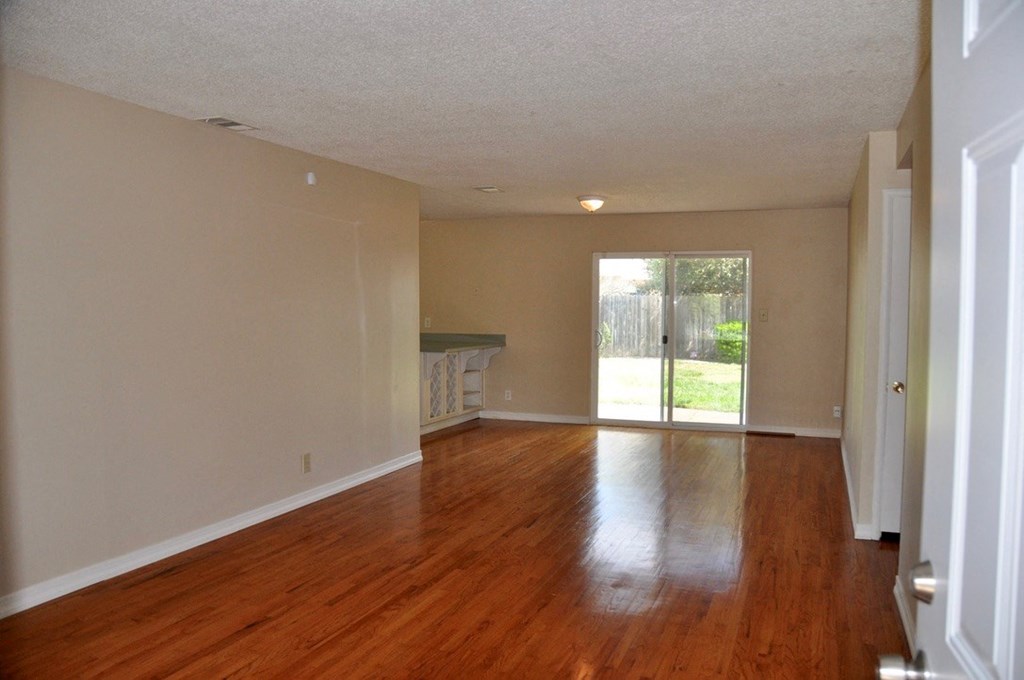 an empty living room with wooden floors and a door to a yard