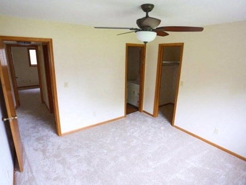 an empty living room with a ceiling fan and three doors