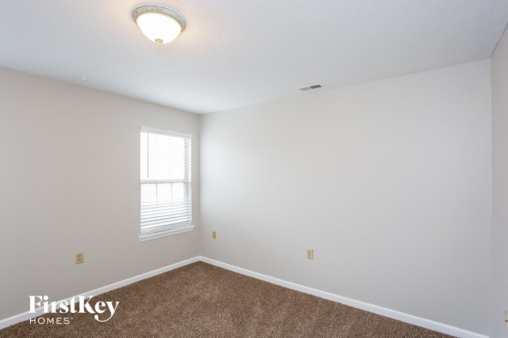 A room with a carpeted floor and a window with blinds.