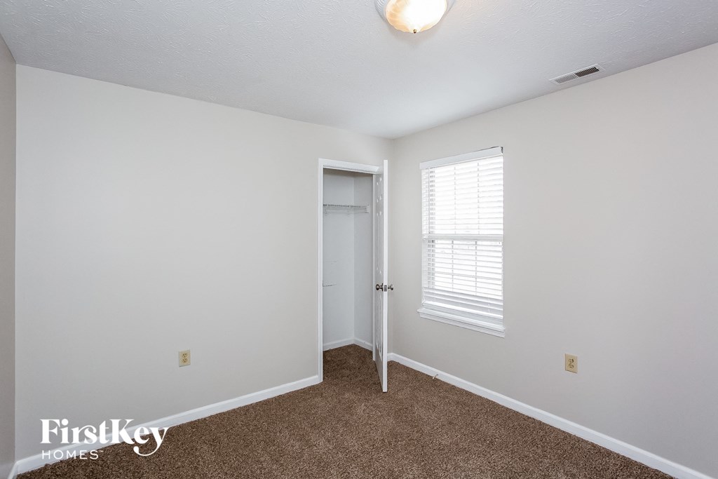 A room with a carpeted floor, a door, and a window with blinds.
