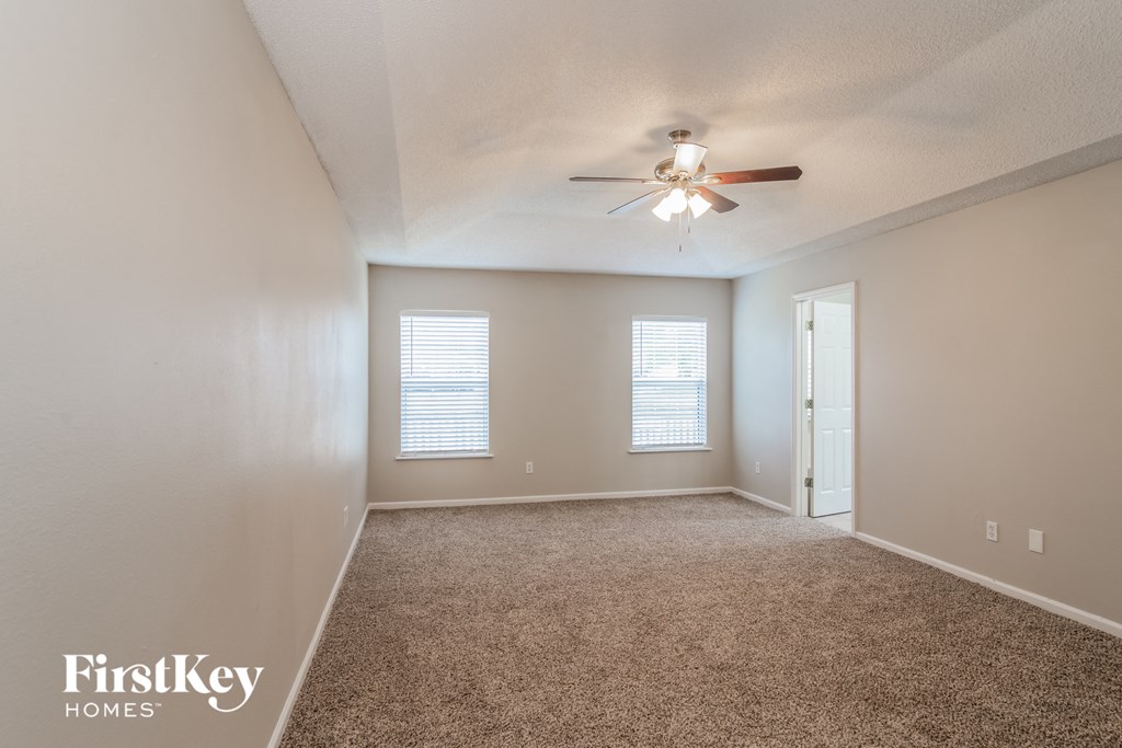 A spacious room with a ceiling fan and two windows.