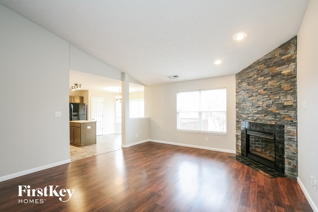 A spacious living room with wood flooring and a stone fireplace.