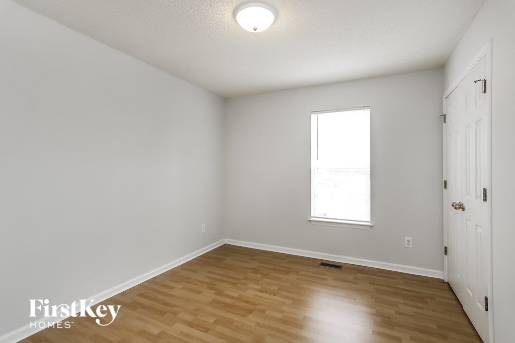 a bedroom with white walls and wood flooring and a window