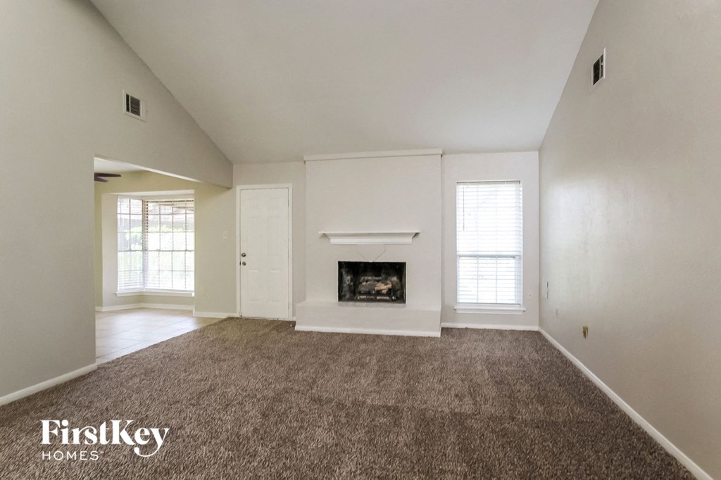 A large, empty room with a fireplace and carpeted floor.