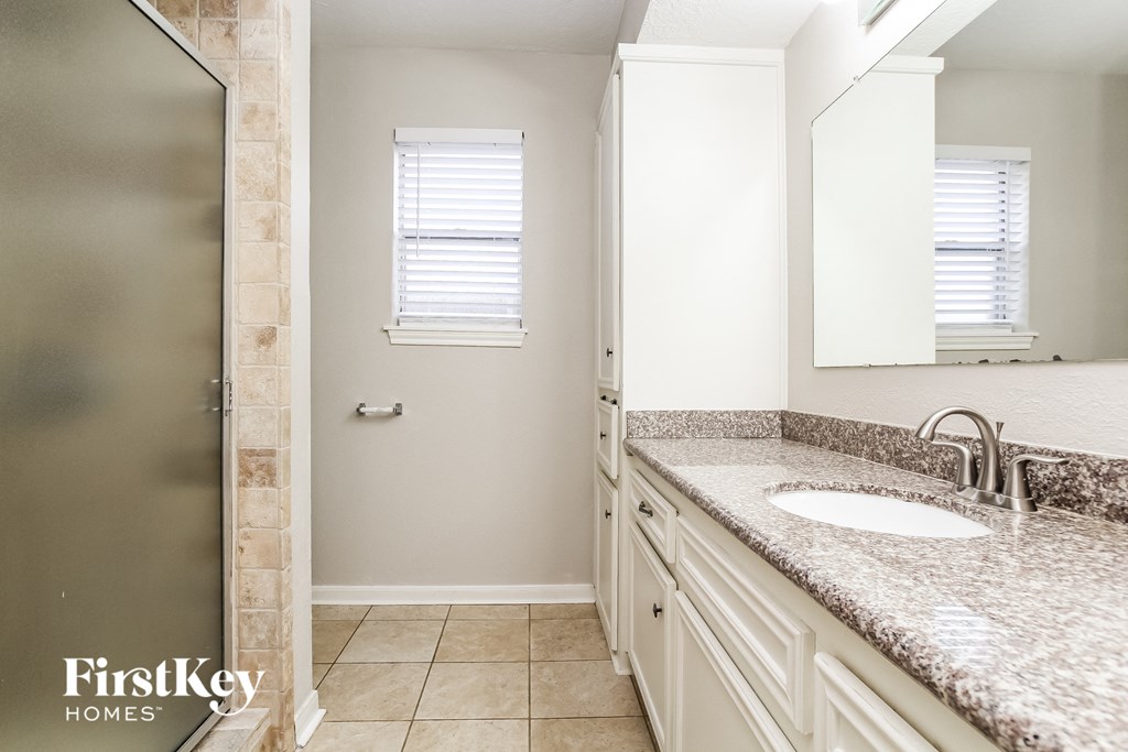 A bathroom with a sink, mirror, and a window with blinds.