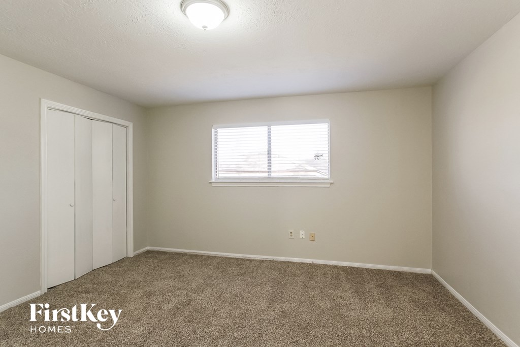 A room with a carpeted floor, a window with blinds, and a door.